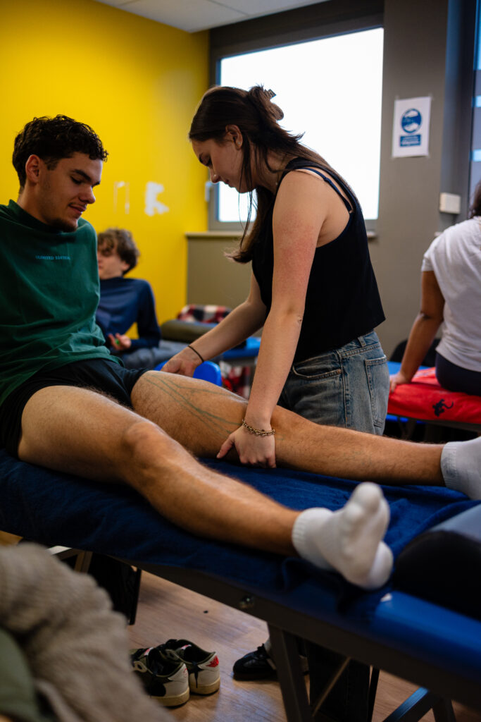 Étudiante palpant la cuisse d'un autre étudiant lors d'un TP d'ostéopathie
